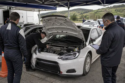 Zona de verificaciones tecnicas de rallye con coches y mecanicos en paddock